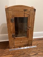 Front view of antique wooden medicine cabinet with glass door and drawer below. Shows wood condition and dimensions with ruler.