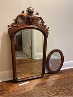 Photo of two antique walnut framed mirrors; one large rectangular with carved top and one smaller oval beveled mirror side by side