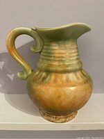 Side angle view showing jug's rounded shape, handle, and orange-green glaze.