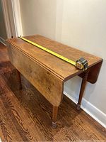 Side view of antique wooden table folded with measuring tape showing length of approximately 42 inches.