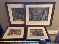 Four antique etchings in original frames arranged on floor with measuring tape to show size, two larger and two smaller pieces visible, lighting shows some frame damage