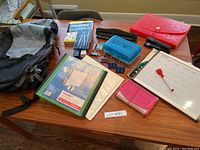 Full top view of all items laid out on wooden table including backpack, stationery, binders, book, pencil cases and whiteboard calendar with marker, showing all back-to-school supplies included in the lot.