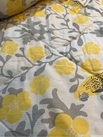 Close-up photo showing quilted yellow, grey and white floral bed cover with visible signs of wear.