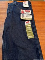 Full view of folded dark blue Wrangler jeans with tags showing brand and fit details.