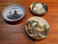 Three collectors' plates shown on a wooden surface, two from Staffordshire China with John Constable artwork, one Royal Copenhagen plate with church scene