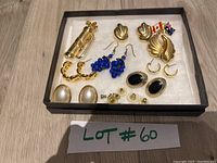 Photo of assortment of earrings in box showing various designs including gold-tone, faux pearls, blue beads, black stones, and flag studs.