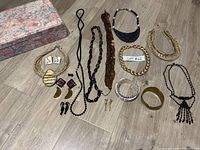 Overview of all jewelry pieces laid out next to floral jewelry box on floor: necklaces, bracelets, earrings in various styles and materials.