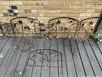 Metal garden border panels laid out, showing decorative bird and floral motifs and metal plant stand beside them.