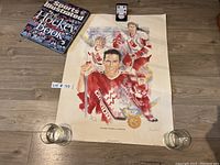 Lot laid out on wood floor showing all items: signed hockey print with coin attached, two glasses, and book