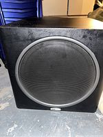 Front view of the Polk Audio PSW125 subwoofer showing the speaker grille and black cabinet.