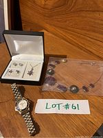 Full view of all lot items on wood surface: Orleans watch, Tivoli set in box, and necklace in plastic bag.