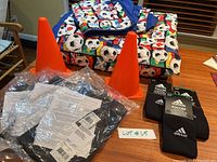 Kids World Cup soccer-themed bedding folded on table with two orange cones, plus packaged Adidas youth medium black shorts in plastic, and small label with lot number.