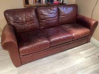 Front view of the brown leather couch showing three seat cushions and worn leather surface.