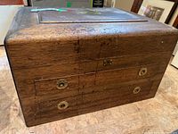 View of the closed wooden box showing brass handles and lock on the front, with visible wood grain and some wear.