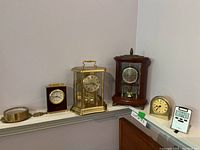 Image of five clocks arranged on shelves showing different styles and materials including brass, wood, and digital design.