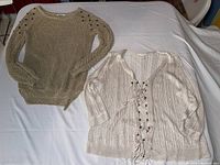 Two knit sweaters laid flat on a white sheet: cream Chico's brand sweater with lace-up front and gold Papaya brand sweater with eyelet shoulder details.