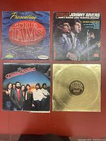 Photo of four vintage vinyl records laid out on a red surface, showing front covers and a gold record.