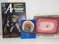 Photo showing Superman Batman comic cover, small owl painting, and abstract painting together