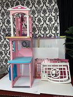 Three-story pink and white dollhouse parts with furniture and decorative features