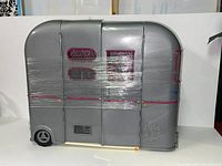 Gray Barbie RV van wrapped in plastic showing exterior with pink and blue detailing.