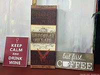 Photo of three kitchen wall art signs featuring coffee, wine, and chocolate themes.