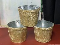 Three gold textured metal pots with bark-like surface, silver interior, arranged in a group