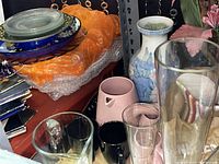 Glass and ceramic items including vases, pitchers, mugs, and plates arranged on shelves.
