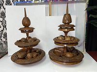 Photo showing a pair of vintage wooden 3-tier fruit-themed lazy susan table toppers with carved fruit and pointed finials.