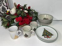 Photo showing the Christmas-themed decorative arrangement with bird figurines, six bowls with Christmas tree designs, six plates with Christmas trees, and four coffee mugs with Christmas tree and gold tree designs.