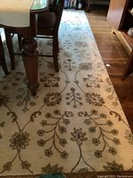 Full length of the area rug under dining table showing floral and vine pattern and texture.