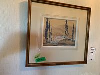 Full view of framed painting on wall showing landscape scene, gold-toned wood frame and cream mat