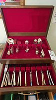 Open two-level wooden case showing upper tray of flatware items against red velvet lining