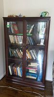 Full front view of the wood cabinet with beveled glass doors showing interior shelves filled with books and other items.
