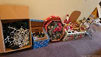Photo showing multiple cardboard boxes on floor containing Christmas decorations including string lights, ornaments, wreath, and timers