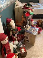 Overall assortment of Christmas decorations including plush Santa, snowman, dog, garlands, stockings and animated village box on carpet