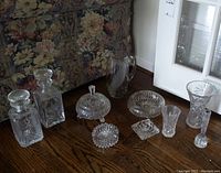 Full shot of the lot showing two decanters, candy dish with lid, three ashtrays, three vases, and jug on wooden floor.