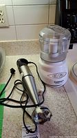 Photo showing the Cuisinart Mini-Prep Plus food processor with lid on and immersion blender lying beside it on a kitchen countertop.