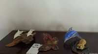 Wide shot showing all figurines including John Perry dolphins on driftwood, metal butterfly, blue glass dolphin, and dog figurine on a table.