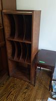 Angle view of the tall wood record cabinet with curved dividers, next to the small wood table, showing overall style and condition.