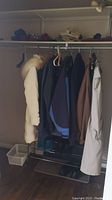 Photo of multiple coats hanging in a closet on hangers, showing varied colors and styles