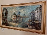 Framed painting on wall showing street scene with buildings and people. Signed by C Andrew.