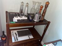 Overview of all items: wooden cart with wine carafes, salt and pepper mills, pewter mug, cheese cutters, napkin rings, and utensils arranged on shelves