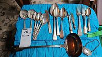Full lot overview showing sterling spoons, spreader, ladle, tongs, picks, letter opener and forks laid out on blue cloth.