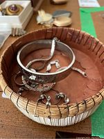 Photo showing three silver bracelets and three rings arranged in a woven basket.