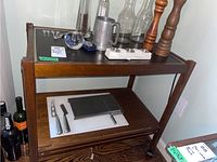 Full view of wooden warming cart with two shelves, various bottles and kitchen tools on and around it.