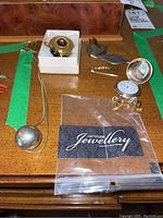 Overview of all items on wood surface including pocket watch with bow pin, garnet style brooch and earrings, pewter brooches, globe necklace, and rhinestone bar brooch