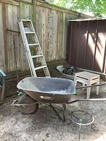 Photo showing 6 ft aluminum step ladder, black Erie metal wheelbarrow, small resin side table, garden rake.
