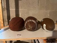 Three worn, autographed footballs from Queens University displayed on a shelf.
