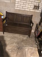 Full view of wooden storage bench showing armrests, paneled backrest, and front storage compartment closed.