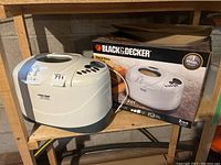 Black & Decker B2300 breadmaker placed on wooden shelf with original box behind it, showing branding and product image